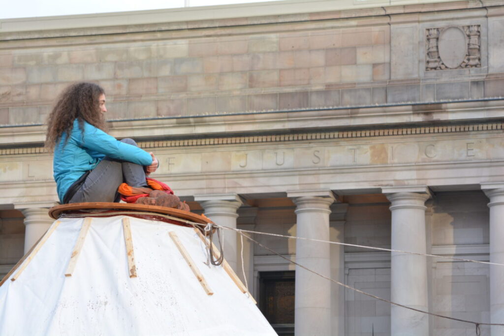350 Seattle divestment campaigner sits atop tarpee in downtown Seattle