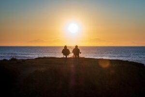 Two retirees sit on the shore gazing at the ocean sunset